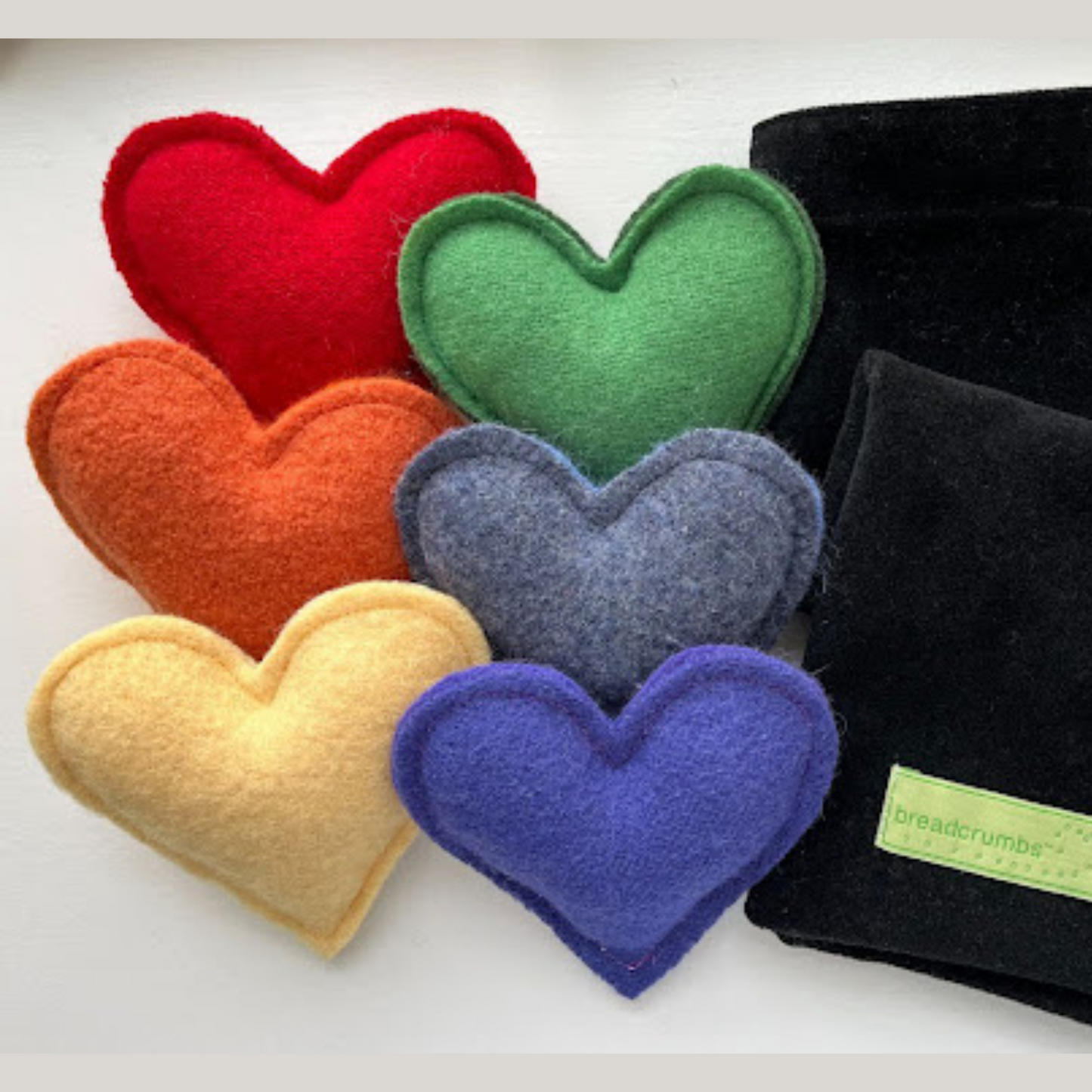 A collection of heart-shaped pillows in various colors including red, green, orange, gray, yellow, blue, and a black bag.
